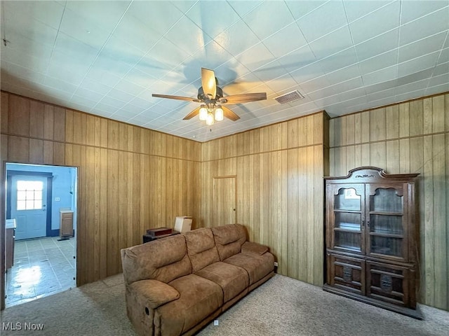 living room featuring ceiling fan, light colored carpet, and wooden walls