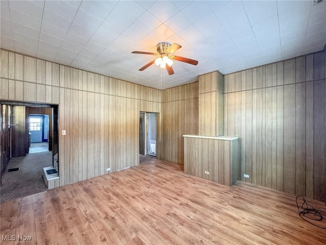 empty room featuring wood walls, hardwood / wood-style floors, and ceiling fan