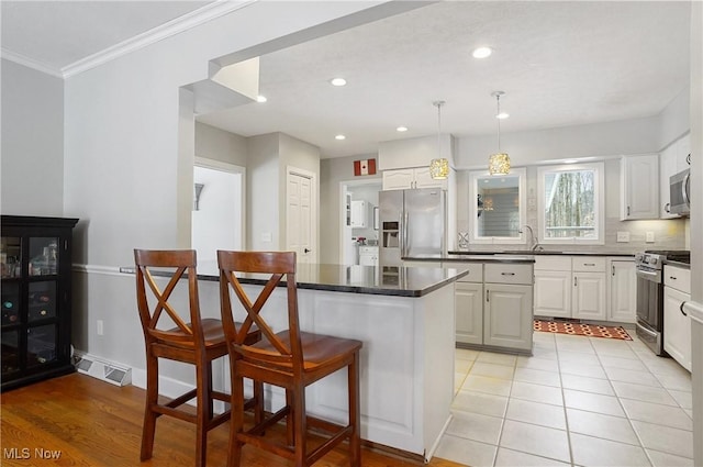 kitchen with white cabinets, sink, decorative light fixtures, stainless steel appliances, and a breakfast bar area