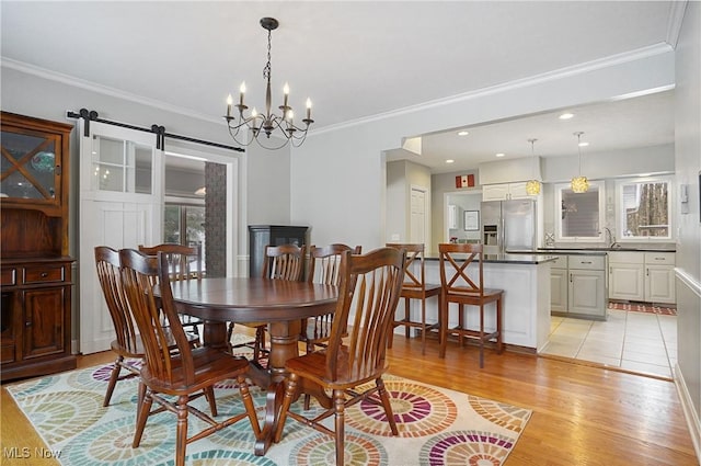 dining space featuring a barn door, sink, light hardwood / wood-style flooring, ornamental molding, and an inviting chandelier