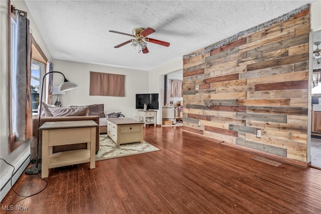 living room with a textured ceiling, wooden walls, dark hardwood / wood-style floors, and ceiling fan