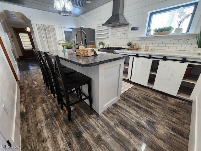 kitchen with a kitchen island with sink, stove, wall chimney range hood, a breakfast bar, and dark hardwood / wood-style floors