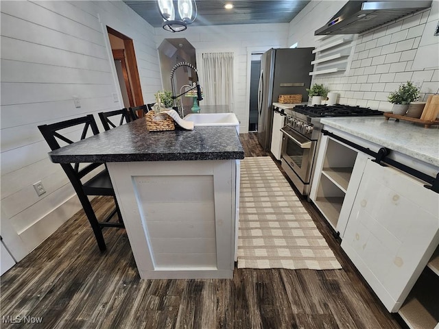 kitchen with wall chimney exhaust hood, stainless steel appliances, sink, a kitchen breakfast bar, and a kitchen island with sink