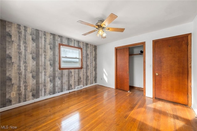 unfurnished bedroom featuring wood walls, hardwood / wood-style flooring, and ceiling fan