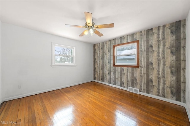 unfurnished room featuring hardwood / wood-style flooring, wooden walls, and ceiling fan