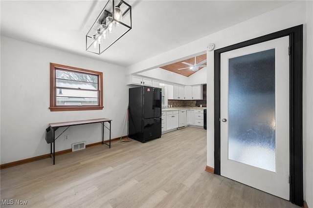 kitchen featuring light hardwood / wood-style floors, tasteful backsplash, white cabinetry, black fridge, and pendant lighting