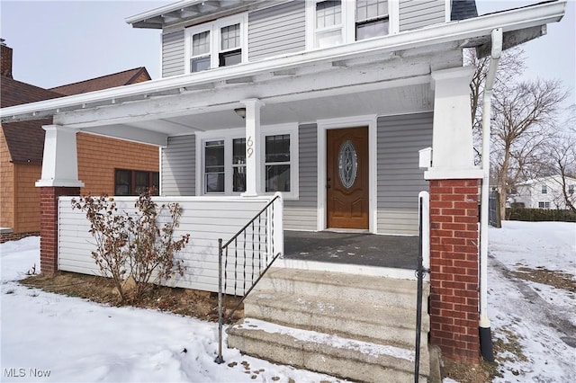 snow covered property entrance with covered porch