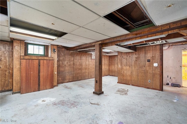 basement with a drop ceiling and wood walls