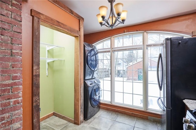 entryway featuring light tile patterned floors, a chandelier, stacked washer and dryer, and brick wall