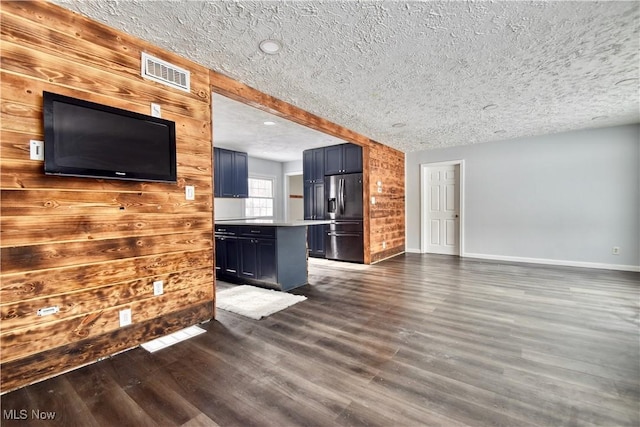 unfurnished living room with a textured ceiling, wooden walls, and dark hardwood / wood-style floors