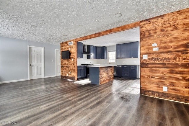 kitchen featuring dark wood-type flooring, wall chimney range hood, blue cabinetry, wood walls, and stainless steel dishwasher