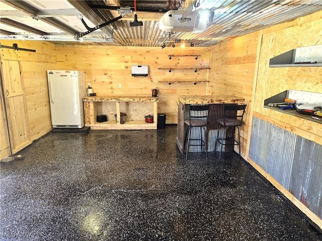 garage featuring white refrigerator, a garage door opener, and wood walls