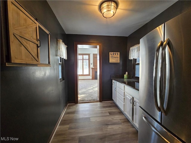 kitchen with stainless steel refrigerator, dark stone countertops, dark hardwood / wood-style floors, and white cabinets