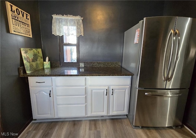 kitchen featuring white cabinetry, dark hardwood / wood-style flooring, stainless steel refrigerator, and dark stone counters