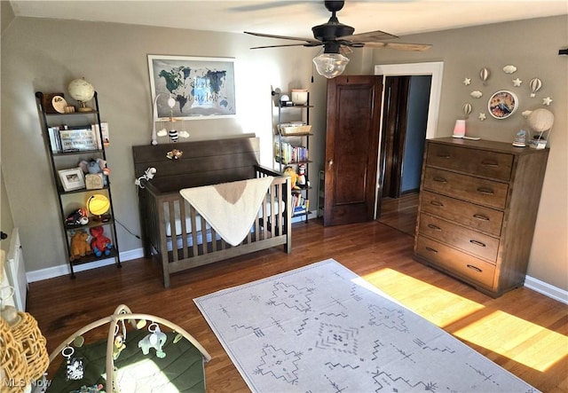 bedroom with ceiling fan, dark hardwood / wood-style floors, and a crib