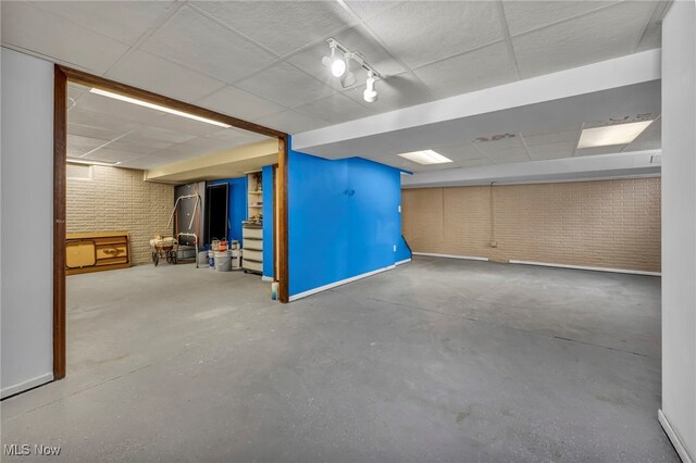 basement with a paneled ceiling and brick wall