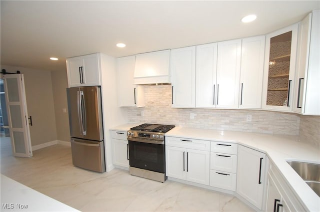 kitchen with white cabinetry, decorative backsplash, stainless steel appliances, a barn door, and custom range hood