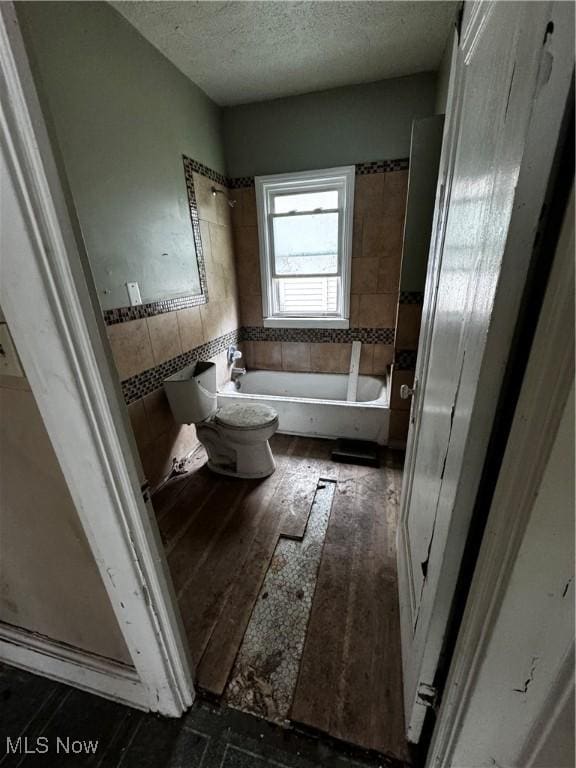 bathroom featuring a textured ceiling, toilet, hardwood / wood-style flooring, and a bath