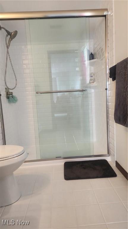 bathroom featuring tile patterned flooring, toilet, and a shower with shower door