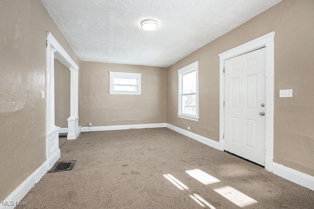 carpeted foyer entrance with a textured ceiling and ornate columns