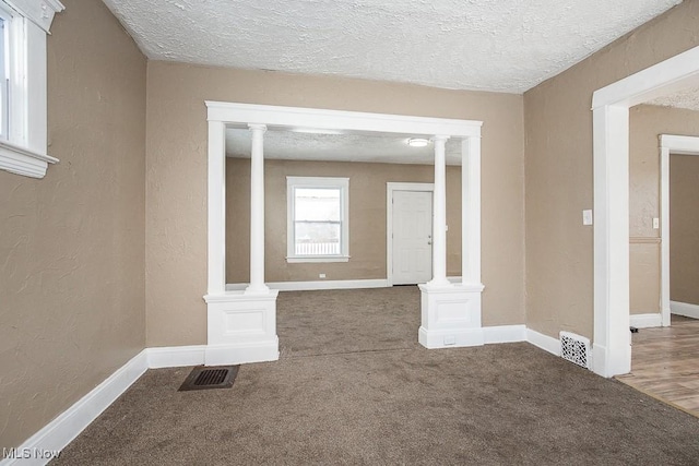 unfurnished room featuring carpet flooring, decorative columns, and a textured ceiling