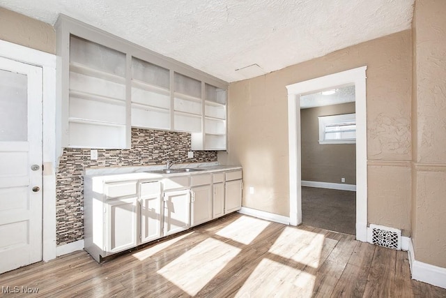 kitchen with sink, white cabinetry, a textured ceiling, light hardwood / wood-style floors, and decorative backsplash