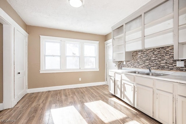 kitchen with a textured ceiling, white cabinets, sink, light hardwood / wood-style flooring, and backsplash