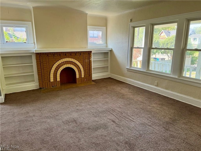 unfurnished living room featuring built in features, a brick fireplace, carpet floors, and a healthy amount of sunlight