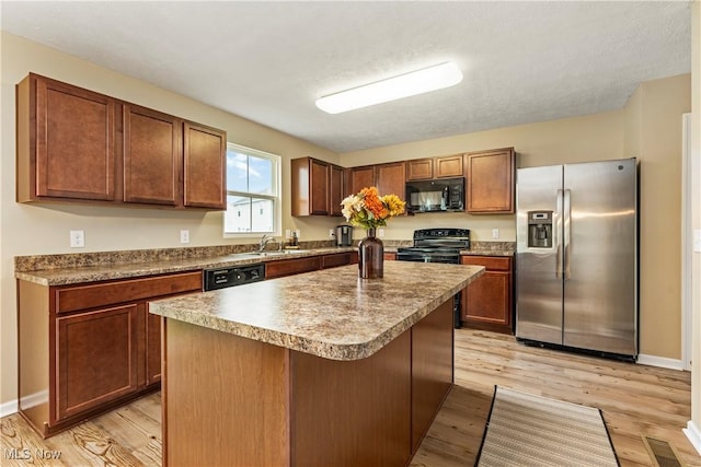 kitchen with black appliances, a center island, a kitchen breakfast bar, light wood-type flooring, and sink