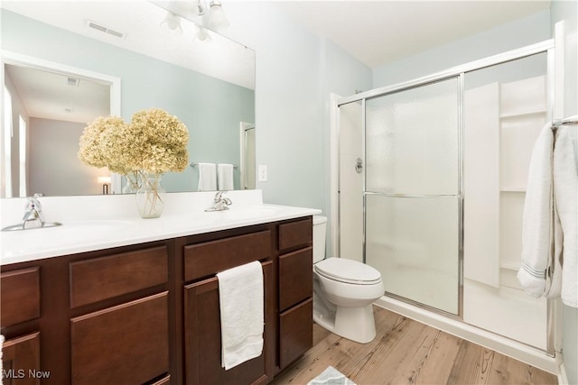 bathroom with hardwood / wood-style floors, toilet, a shower with shower door, and vanity