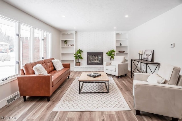 living room featuring built in shelves, light wood-type flooring, and a brick fireplace