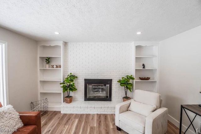 living area with a brick fireplace, a textured ceiling, and light wood-type flooring