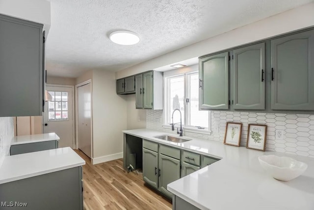 kitchen with green cabinetry, decorative backsplash, sink, light wood-type flooring, and kitchen peninsula