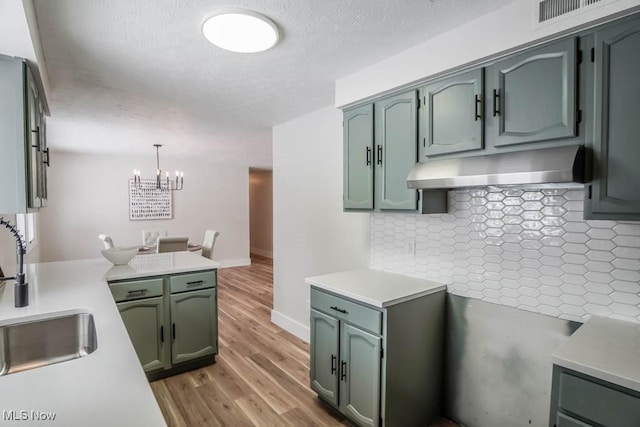 kitchen with sink, decorative light fixtures, backsplash, exhaust hood, and a chandelier