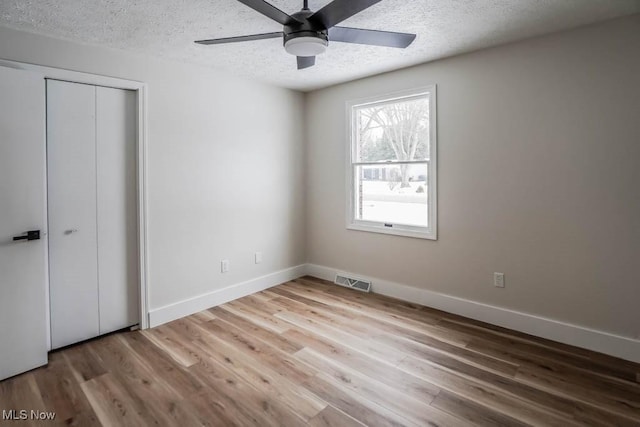 unfurnished bedroom with a closet, a textured ceiling, light hardwood / wood-style flooring, and ceiling fan