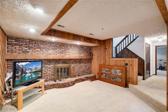 carpeted living room featuring a textured ceiling, wood walls, and a fireplace