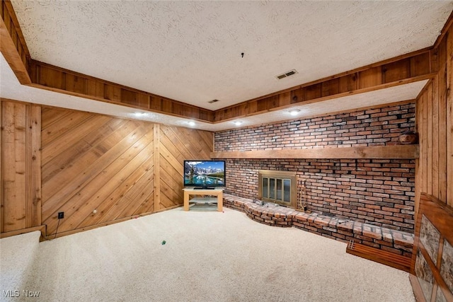 unfurnished living room featuring wood walls, carpet flooring, a textured ceiling, and a brick fireplace