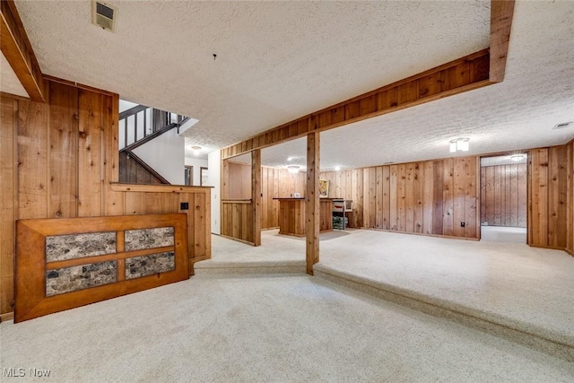 basement featuring wood walls, a textured ceiling, and light carpet