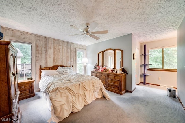 carpeted bedroom featuring ceiling fan, wood walls, a textured ceiling, and multiple windows