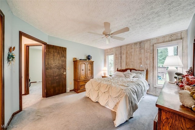 carpeted bedroom with ceiling fan, wooden walls, a textured ceiling, and multiple windows