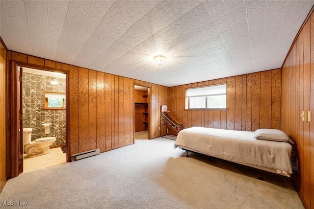 carpeted bedroom featuring wooden walls, a baseboard heating unit, and ensuite bathroom