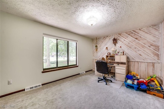 office area featuring carpet, wooden walls, and a textured ceiling