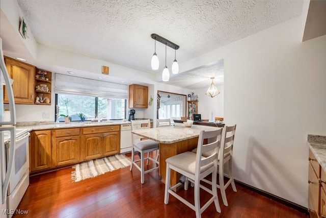 kitchen featuring white appliances, dark wood-type flooring, hanging light fixtures, kitchen peninsula, and a breakfast bar