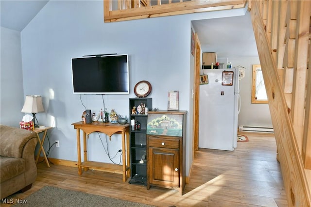 interior space featuring a baseboard heating unit, vaulted ceiling, and light hardwood / wood-style floors