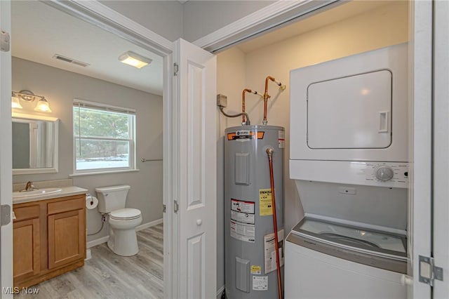 clothes washing area featuring sink, light wood-type flooring, water heater, and stacked washing maching and dryer