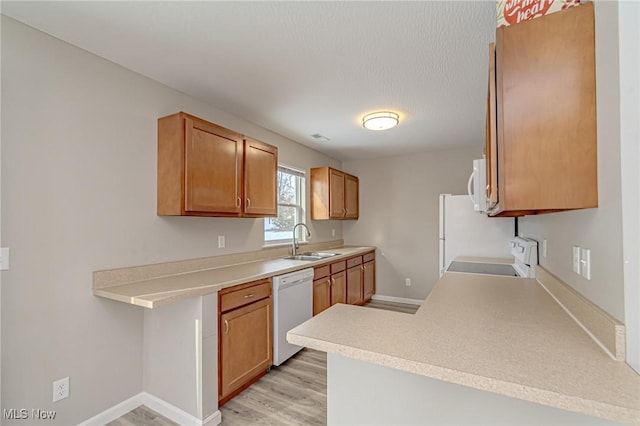 kitchen featuring sink, white appliances, light hardwood / wood-style flooring, and kitchen peninsula