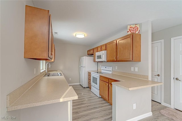 kitchen with sink, white appliances, kitchen peninsula, and light wood-type flooring