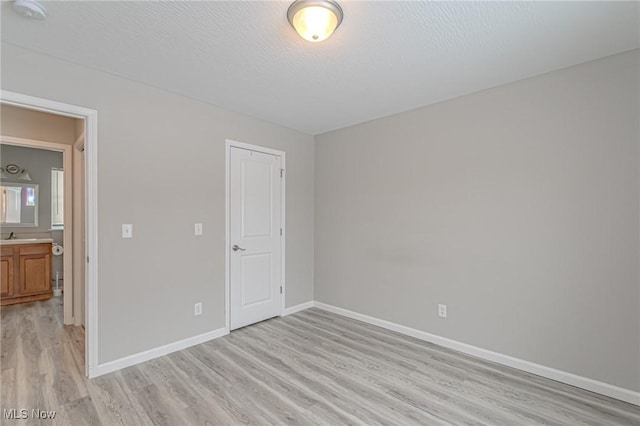 unfurnished bedroom with a textured ceiling, light hardwood / wood-style flooring, and ensuite bath