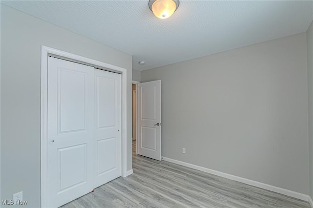 unfurnished bedroom with light hardwood / wood-style floors, a textured ceiling, and a closet