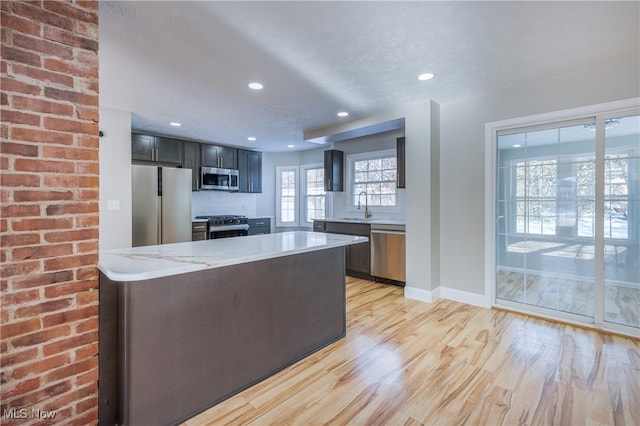 kitchen featuring appliances with stainless steel finishes, light hardwood / wood-style floors, sink, backsplash, and light stone counters